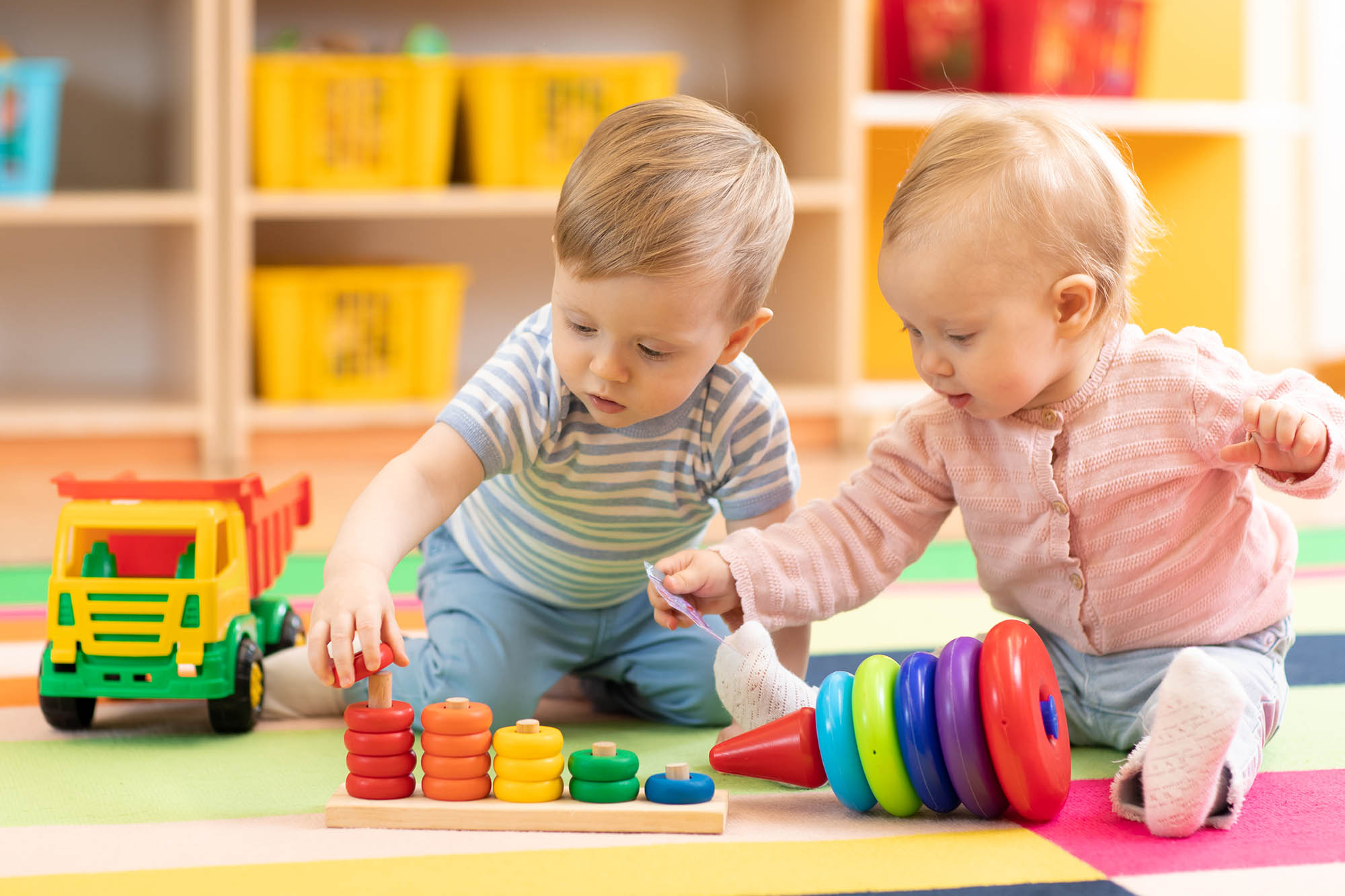 Two toddlers playing with blocks on the floor.